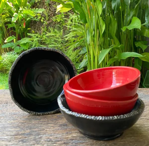 Two glossy red bowls stacked inside a textured black bowl, with a second black bowl standing behind them.