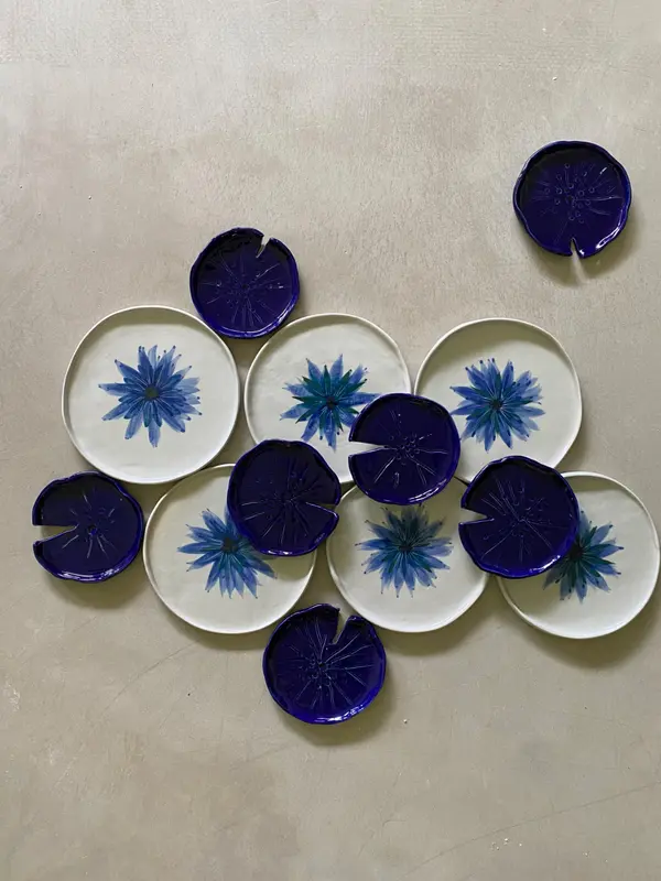 Arrangement of white plates with blue floral designs and dark blue lily pad-shaped ceramic pieces.