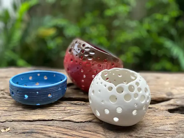Three perforated ceramic candle holders in blue, red, and white glazes on a rustic wooden surface.