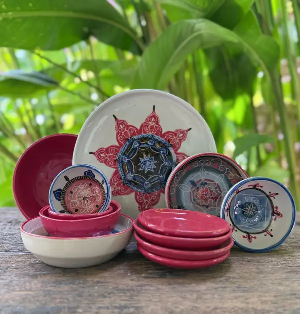 A collection of hand-painted ceramic bowls and plates with red and blue mandala patterns on a wooden surface.