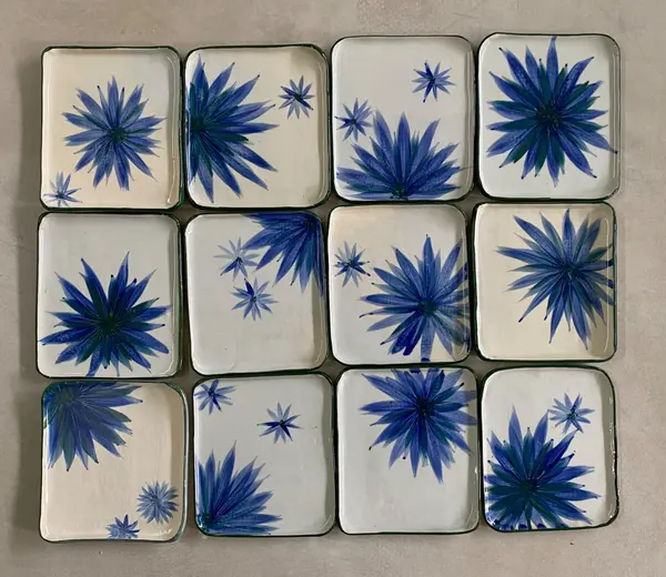 Twelve rectangular white ceramic plates with hand-painted blue floral designs arranged in a grid pattern.