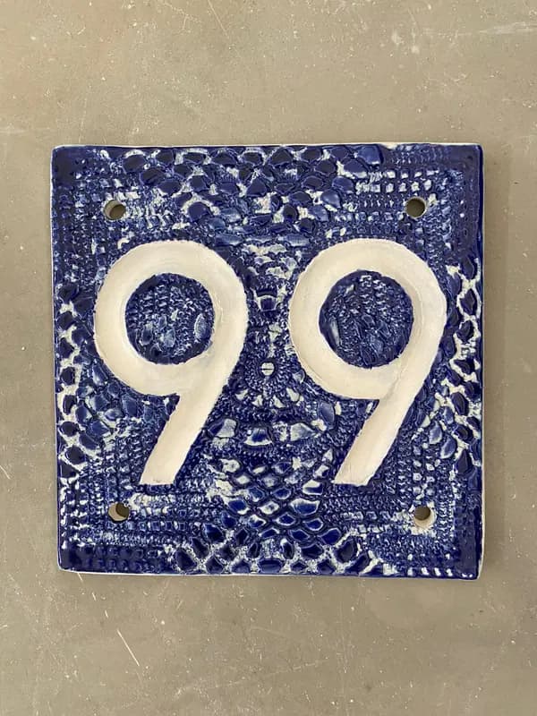 Square ceramic house number tile with white raised numbers 99 on a textured cobalt blue glazed background.