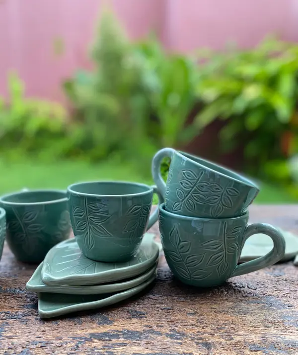 Sage green mugs and leaf-shaped saucers featuring embossed foliage on a rustic wooden table.