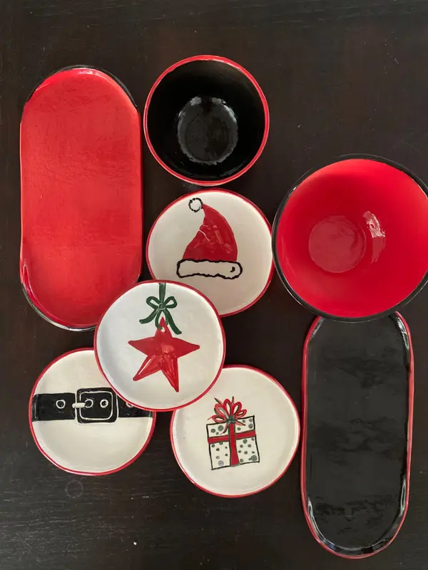 Red, black, and white ceramic bowls, platters, and small plates with hand-painted Christmas illustrations.