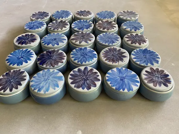 A collection of small light blue ceramic jars with hand-painted blue and purple flowers on the lids.