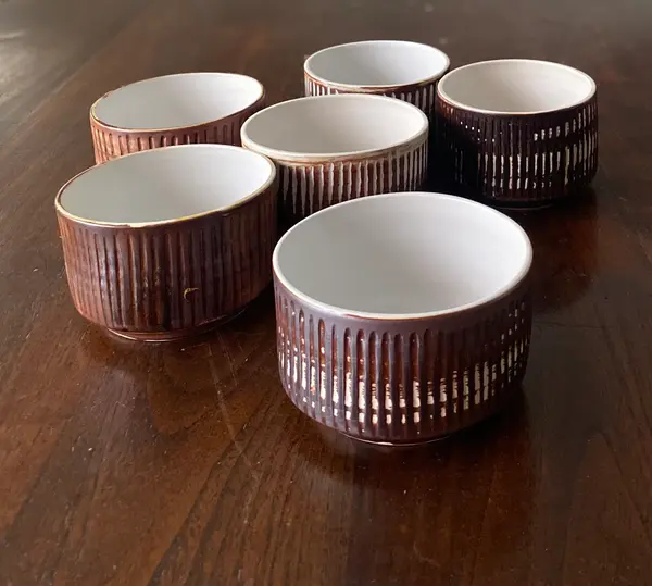 Six small ceramic bowls with dark brown fluted exteriors and white interiors on a dark wood table.