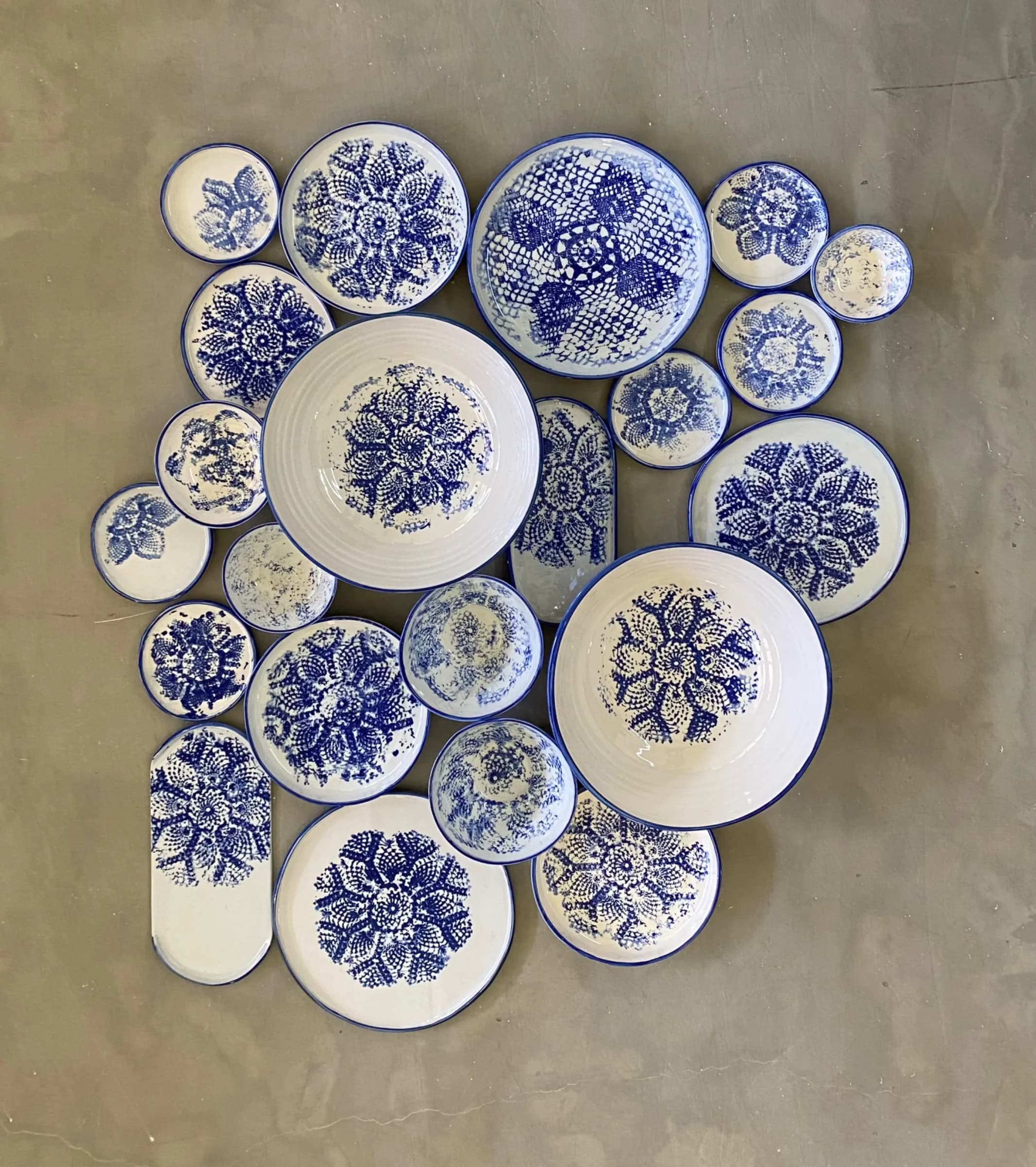 Collection of white and cobalt blue ceramic plates and bowls with intricate lace-like mandala patterns.